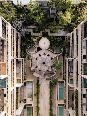 Un edificio residencial de varios pisos con un patio central que incluye una fuente decorativa, rodeado de balcones con plantas.