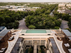 A rooftop pool with a view of a cityscape, surrounded by lush greenery. - Alma Del Cielo Luxe Penthouse Aldea Zama (Tulum)