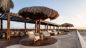 Une terrasse en bois agrémentée de parasols en chaume, de chaises longues et d’un espace piscine.