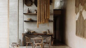 Un espace repas comprenant une table et des chaises en bois, un luminaire suspendu et un mur agrémenté d’étagères et d’objets décoratifs.