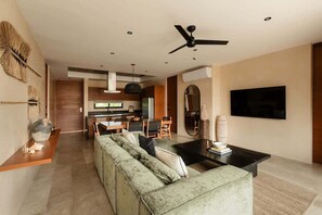 A modern living room with a sofa, a coffee table, a TV, and a ceiling fan. - Alma Del Cielo Luxe Penthouse Aldea Zama (Tulum)