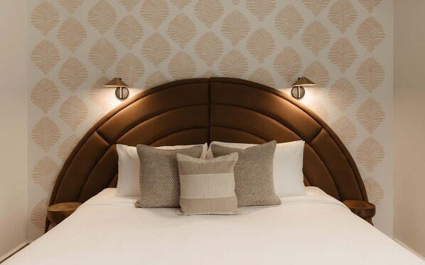 A bed with a brown headboard, two wall-mounted lamps, and patterned wallpaper.