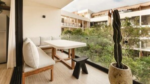 Uma varanda com mesa e cadeiras, um vaso de planta e vista para um pátio com edifícios.