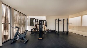 Ein Fitnessraum mit Trainingsgeräten, einem Stehrad und einem Gewichtständer.