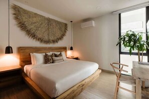 Un dormitorio con cama, lámparas de noche, un cabecero de madera, un tapiz tejido grande, una planta en maceta y vistas a través de una ventana.
