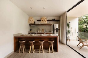 A modern kitchen with a central island, bar stools, pendant lights, and a view of greenery outside. - K'Abax Jungle Apartment Beach Club Access (Tulum)