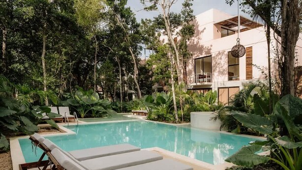 A pool with lounge chairs, surrounded by lush greenery and a modern building.