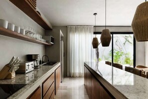 A modern kitchen with a central island, wooden cabinets, and a built-in microwave. - Villa Coralia J2 Private Pools Beach Club Access (Tulum)