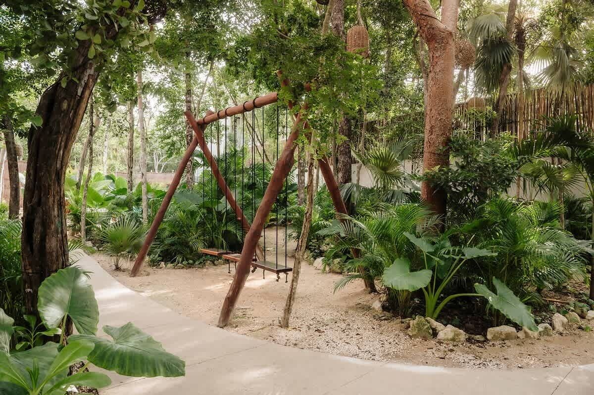 A garden with a swing set, trees, and various plants.
