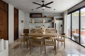 A modern dining area with a wooden table and chairs, a ceiling fan, and a kitchen in the background.