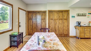 Une pièce dotée d’un plancher en bois, d’une table recouverte d’une nappe à motifs floraux, d’un buffet en bois et d’une fenêtre donnant sur un paysage verdoyant.