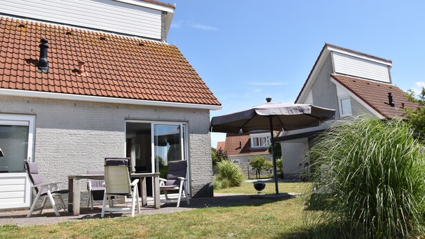 A residential property with a tiled roof, a patio with outdoor furniture, and a covered seating area.