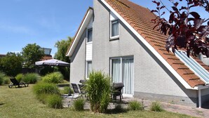 A modern house with a sloped roof, a patio with outdoor furniture, and a garden area.