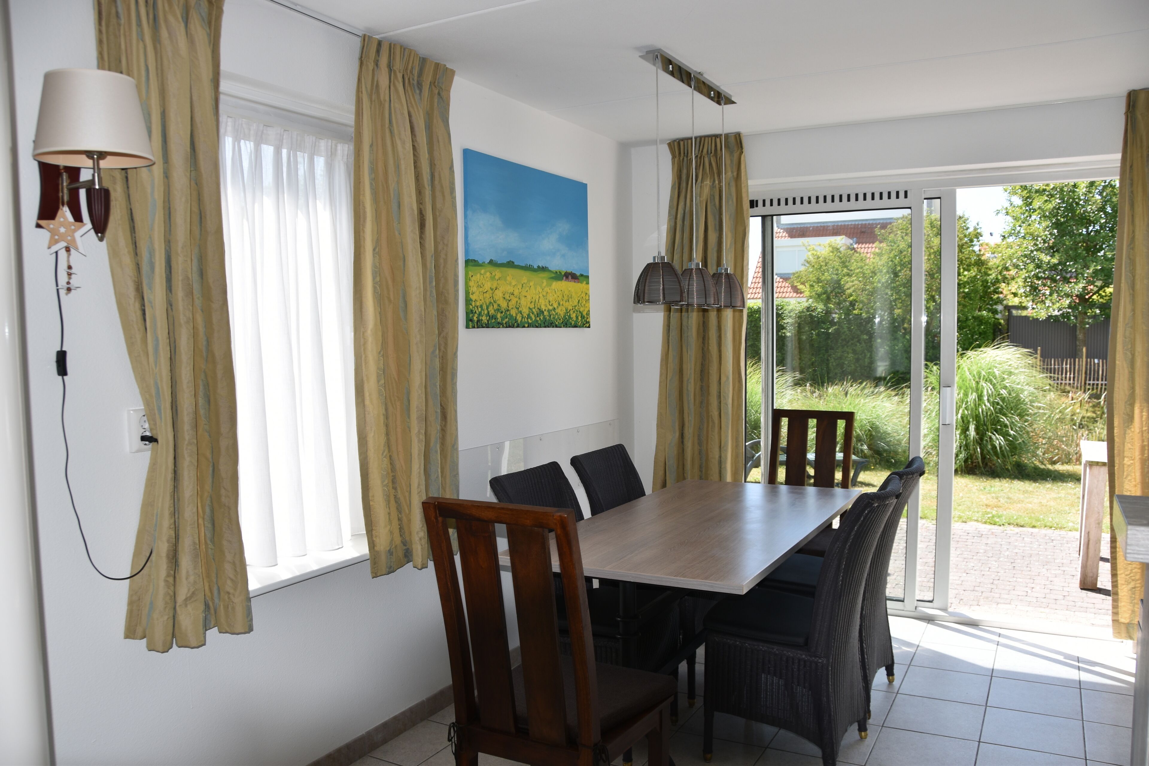A dining area with a wooden table and chairs, a painting on the wall, and curtains on the windows.