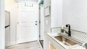 Una cocina compacta con puerta blanca, un lavamanos de acero inoxidable y un salpicadero de azulejos.