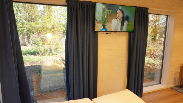 A bedroom with a bed, a TV mounted on the wall, and a large window with curtains.