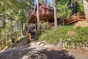 Una baita in legno con una veranda in legno e una scala che vi conduce, immersa tra gli alberi.