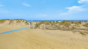 Une plage de sable bordée d’une clôture en bois et un chemin bleu qui mène à l’eau.
