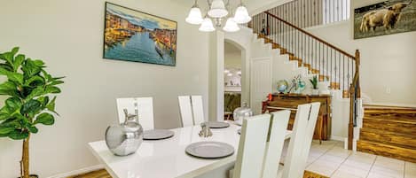 Uma área de refeições com uma mesa branca posta para quatro pessoas, um candelabro e uma escada que leva a um segundo andar.