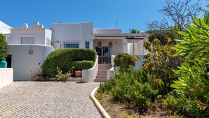 A white building with a cobblestone path leading to a door, surrounded by greenery.