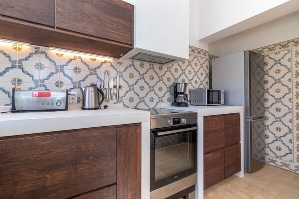 A modern kitchen with wooden cabinets, a built-in oven, a coffee maker, and a microwave. - Casa Amoreira - 2 bed villa on resort with swimming pools, a short walk from to beach, town & amenities (Carvoeiro)