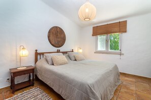 Un dormitorio con cama, lámparas de noche, un reloj de pared, una ventana con vistas y una lámpara colgante.