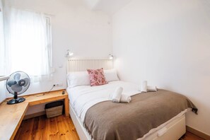 Una camera da letto con un letto, una scrivania, una ventola e un termosifone.