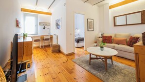 Una sala de estar moderna con suelo de madera, un sofá blanco, una mesa de centro y una zona de comedor con mesa y sillas de madera.