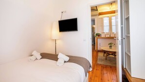 Habitación de hotel con una cama, un televisor, una lámpara y vistas al baño y la cocina a través de una puerta abierta.