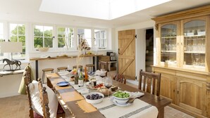 A dining area with a long wooden table, chairs, a chandelier, and a large wooden cabinet with glass doors.