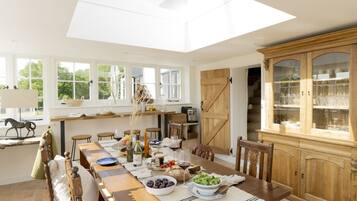 Un comedor con una larga mesa de madera, sillas, una araña y un mueble de madera grande con puertas de cristal.