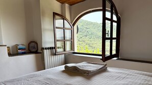 Una camera da letto con un letto, un termosifone, uno scaffale con libri e una finestra vista verde.