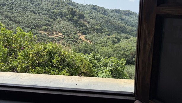 Vista dalla finestra su un paesaggio collinare, con una chiesa in cima a una collina e una torre dell'alta tensione sullo sfondo.