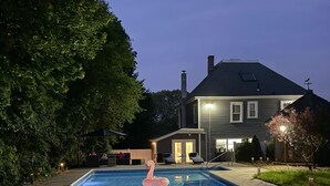 A rectangular swimming pool with a pink flamingo float in the center, surrounded by a concrete deck. - A Charming House with Private Pool & BBQ Area (Dracut)