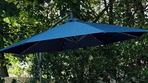 An outdoor seating area with a blue umbrella, wicker furniture, and red cushions. - A Charming House with Private Pool & BBQ Area (Dracut)