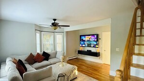 A living room with a white sofa, a coffee table, and a TV mounted on the wall. - A Charming House with Private Pool & BBQ Area (Dracut)