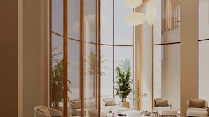 A modern lobby with a large open space, seating area with sofas and chairs, a central coffee table, and a large window with a view of greenery.