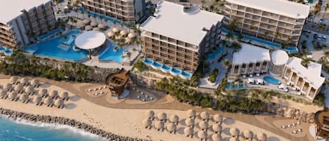 A resort with multiple buildings, a large swimming pool, and a beach area with sun loungers.