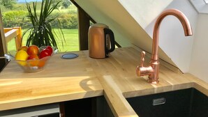 A kitchen with a copper faucet, a bowl of fruit, and a kettle on a wooden countertop.