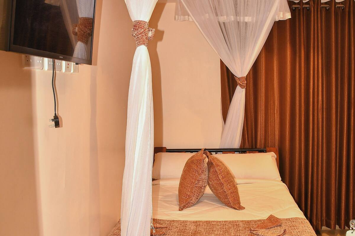 A bedroom with a bed, a TV mounted on the wall, and a bedside table with a phone.