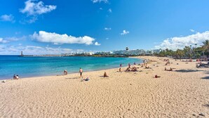 Una playa con gente tomando el sol y nadando, un muelle al fondo, y un edificio de resort.