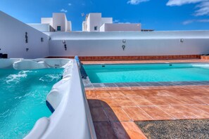 Ein Swimmingpool mit einer weißen Liegefläche und Blick auf weiße Gebäude im Hintergrund.