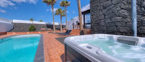 A swimming pool with a hot tub, surrounded by palm trees and stone walls.