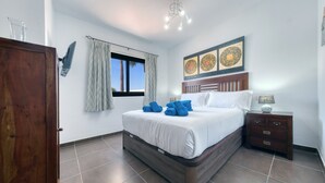A bedroom with a bed, a nightstand, a wooden wardrobe, a window with curtains, and a ceiling light fixture.