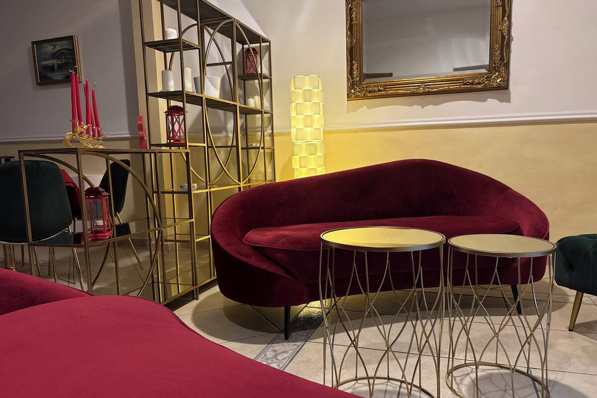 Una habitación con un sofá de terciopelo rojo, una mesa redonda y un espejo con marco dorado.