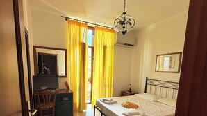 Un dormitorio con cama, escritorio, silla, televisor y ventana con cortinas.