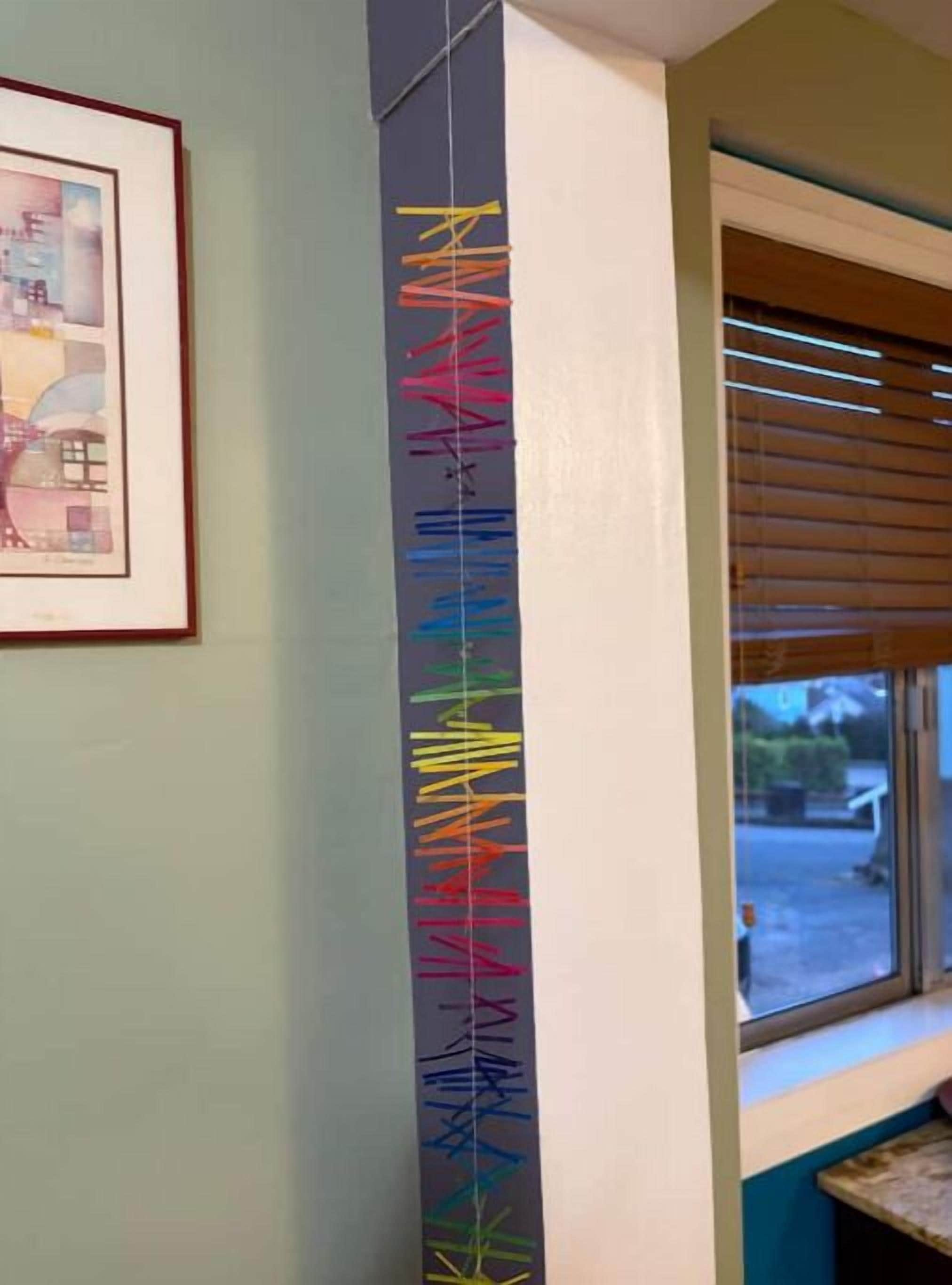A vertical strip of colorful lines on a wall, a framed picture to the left, and a window with blinds to the right.