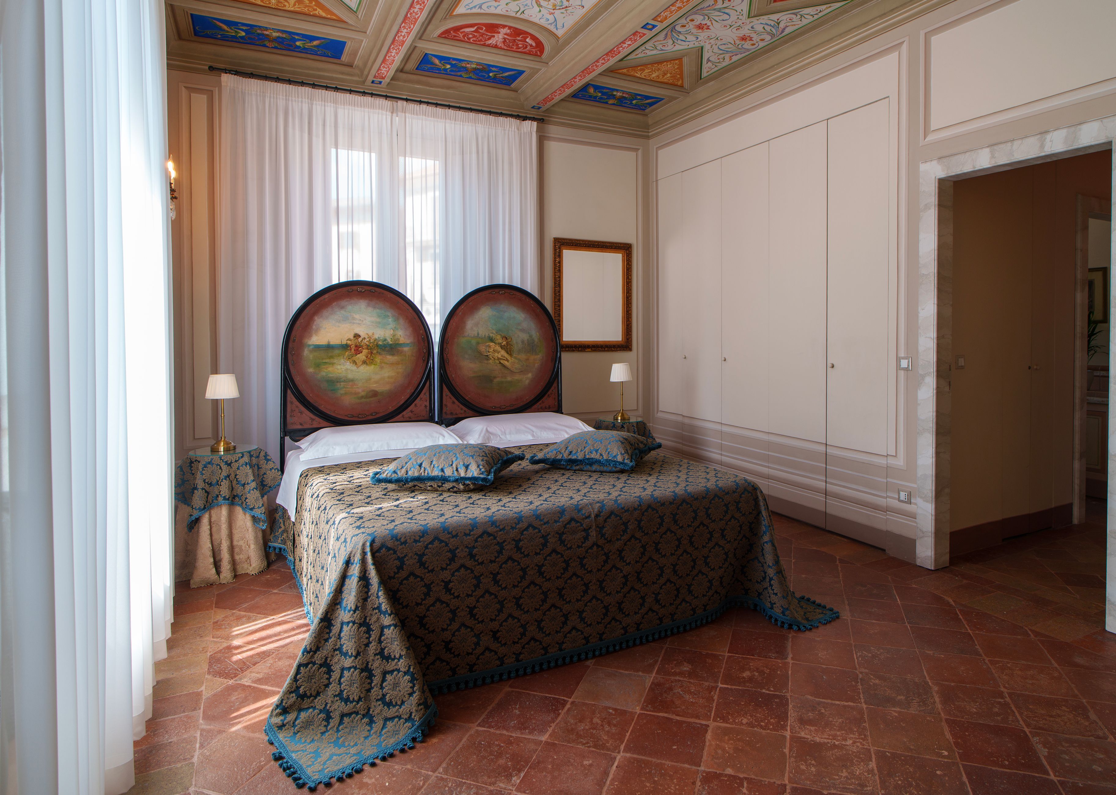 Ein Schlafzimmer mit einem großen Bett, zwei an der Wand befestigten Bildern, einem weißen Vorhang und einem gefliesten Boden.