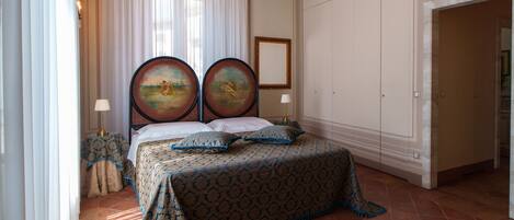 Une chambre à coucher avec un grand lit, deux tableaux accrochés au mur, un rideau blanc et un sol carrelé.