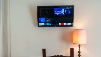 Een flatscreen-tv aan de muur waarop een film draait, een lamp op een tafel en een stoel met een notitieboekje.